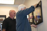KSBA Print/Operations Manager Jeff Million (left) and facilities technician Walt Grabon were in charge of creating the display of nearly two dozen pieces of artwork in KSBA’s largest conference room. VSAKY has enabled students and adults with disabilities to develop their artistic talents for 41 years.