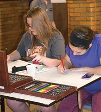 Sophomores Taylor Hill (left) and Andrea Davis work on drawings at one of several tables set up in the hallways where students produced sketches, paintings and designs. Event coordinator Jennifer McMillen said one-quarter of the district’s students were involved in the evening, which also included choral and band performances.