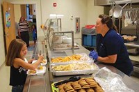 Campbell Elementary cafeteria staffer Ann Fenney kept busy serving up hot dogs, chips and cookies to returning students like Bryna Wellman (left) and Carly Fannin. After the orientation sessions, a mobile food truck with snow cones capped off the evening for youngsters and parents at both schools.