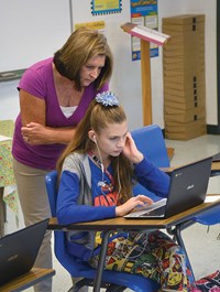 Bernie Carroll-Haney, a language arts teacher, observes seventh-grade student Lauren Souther as she works on a laptop.