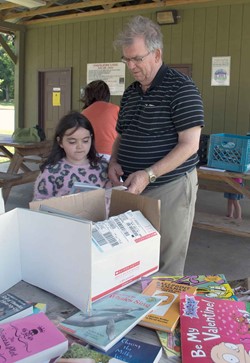 Caverna Independent school board Chairman Wayne Hatcher helps his granddaughter Rebecca Piercy sort through the reading possibilities at the Horse Cave City Park, where the district set up its mobile summer reading program.