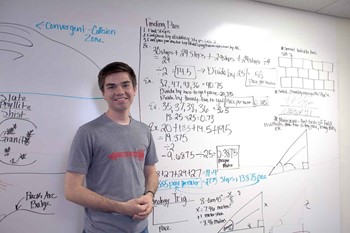 Zeb Hart in front of a dry erase board where students have worked on some calculations.