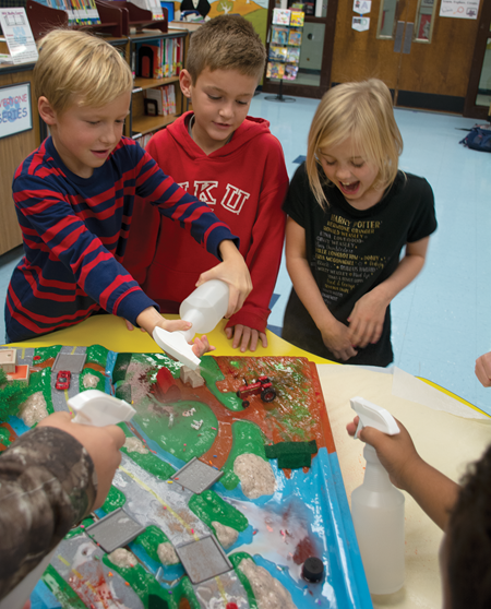 To simulate rain, students sprayed water on the EnviroScape and watched the pollution flow to the streams and ponds. McKenna Carrol, right, and Bryce Davis watch as Ryan Jordan, left, squirts water onto the model.