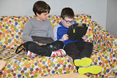 Moyer Elementary students James Owen Taylor (left) and Colin Davis work on tablets on a couch in the school’s hallway.