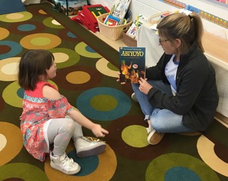 Dayton Independent preschool teacher Anna Kennedy shows the book “Abiyoyo” to student Deanndra Harris. (Photo courtesy of Dayton Independent Schools)